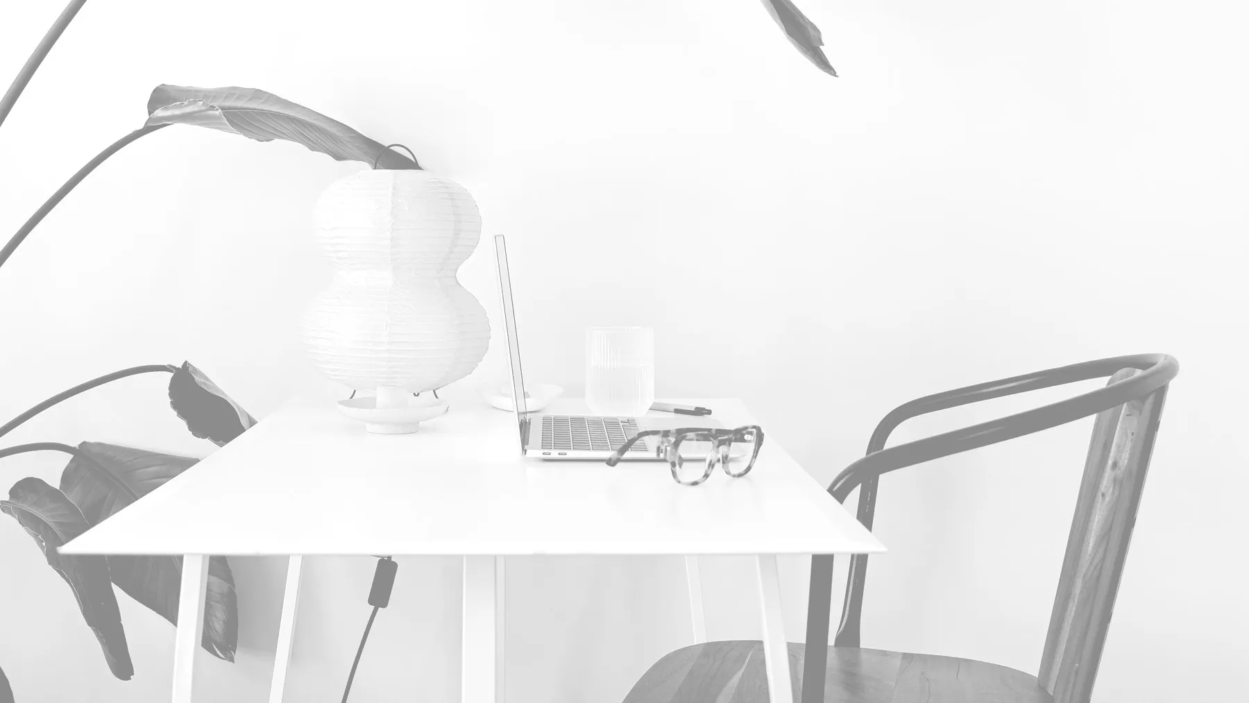 Minimalistisch thuiskantoor met een laptop op een tafel, een plant en een bril